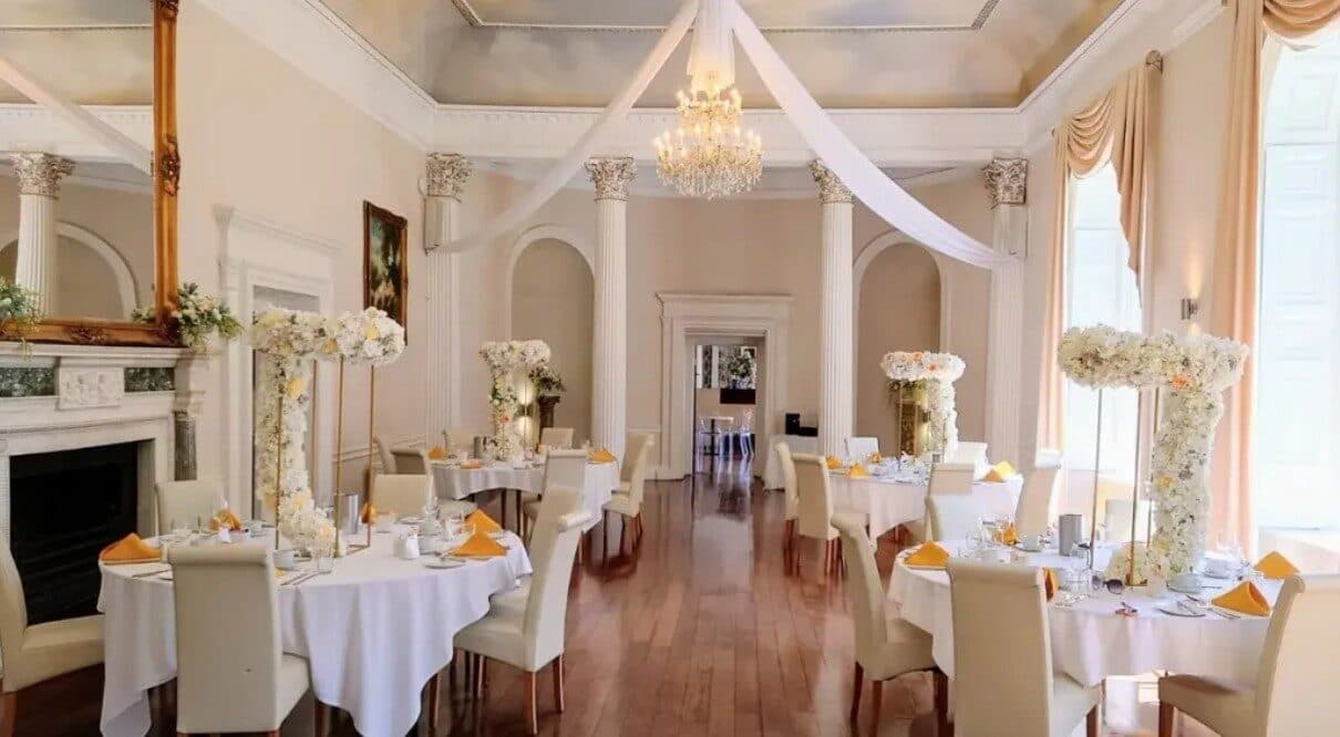 Ivory function room with white draped ceiling, round tables in white linen and tall floral centrepieces