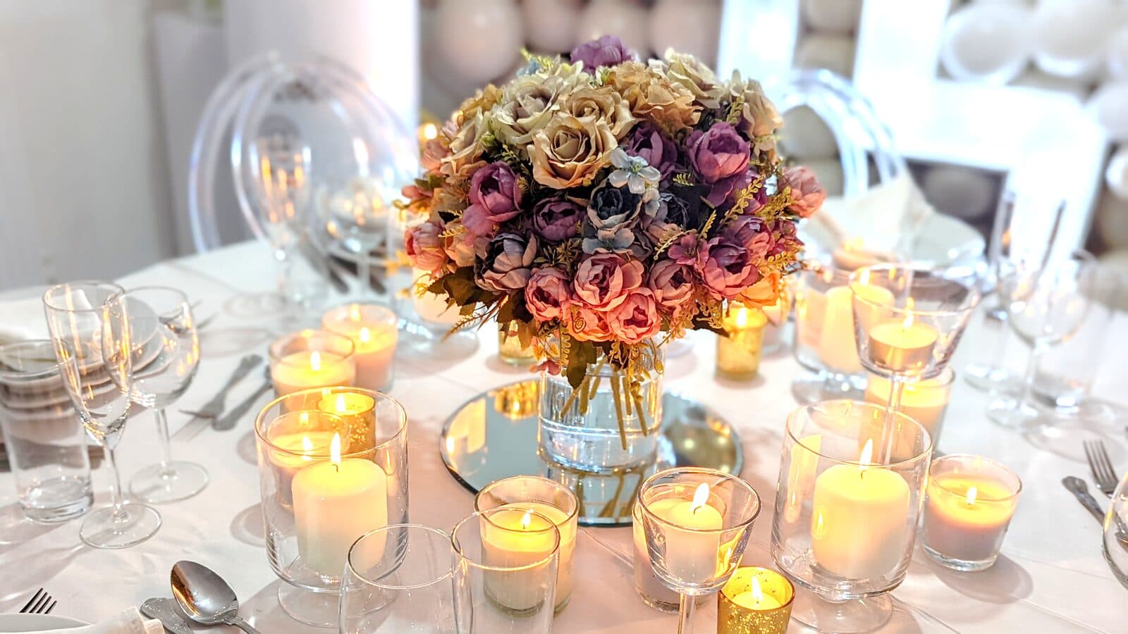 Autumn-toned rose centrepiece surrounded by glass tea light holders and glassware