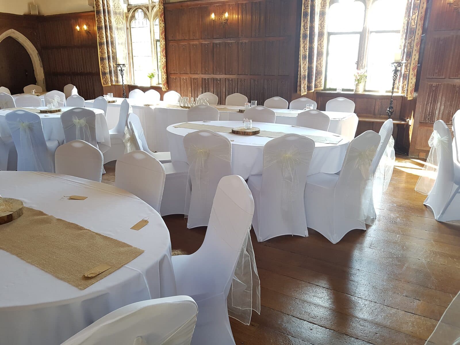Oak-panelled room at Lympne Castle with white chair covers, ivory sashes and hessian table runners
