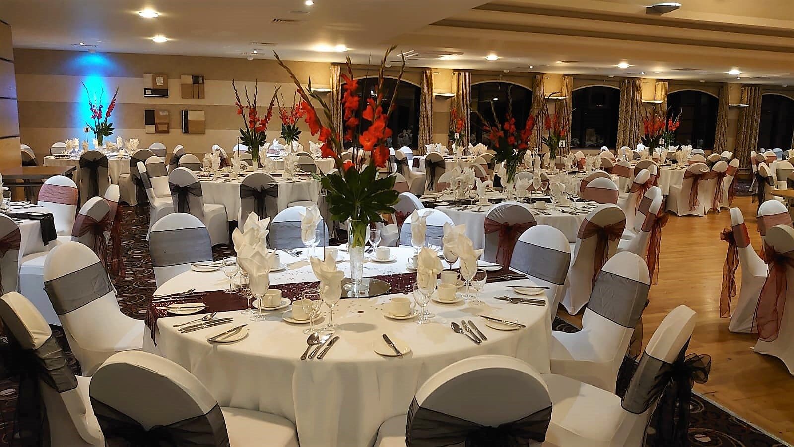 Tables with ivory cloths, dark chair sashes and tall red flower centrepieces