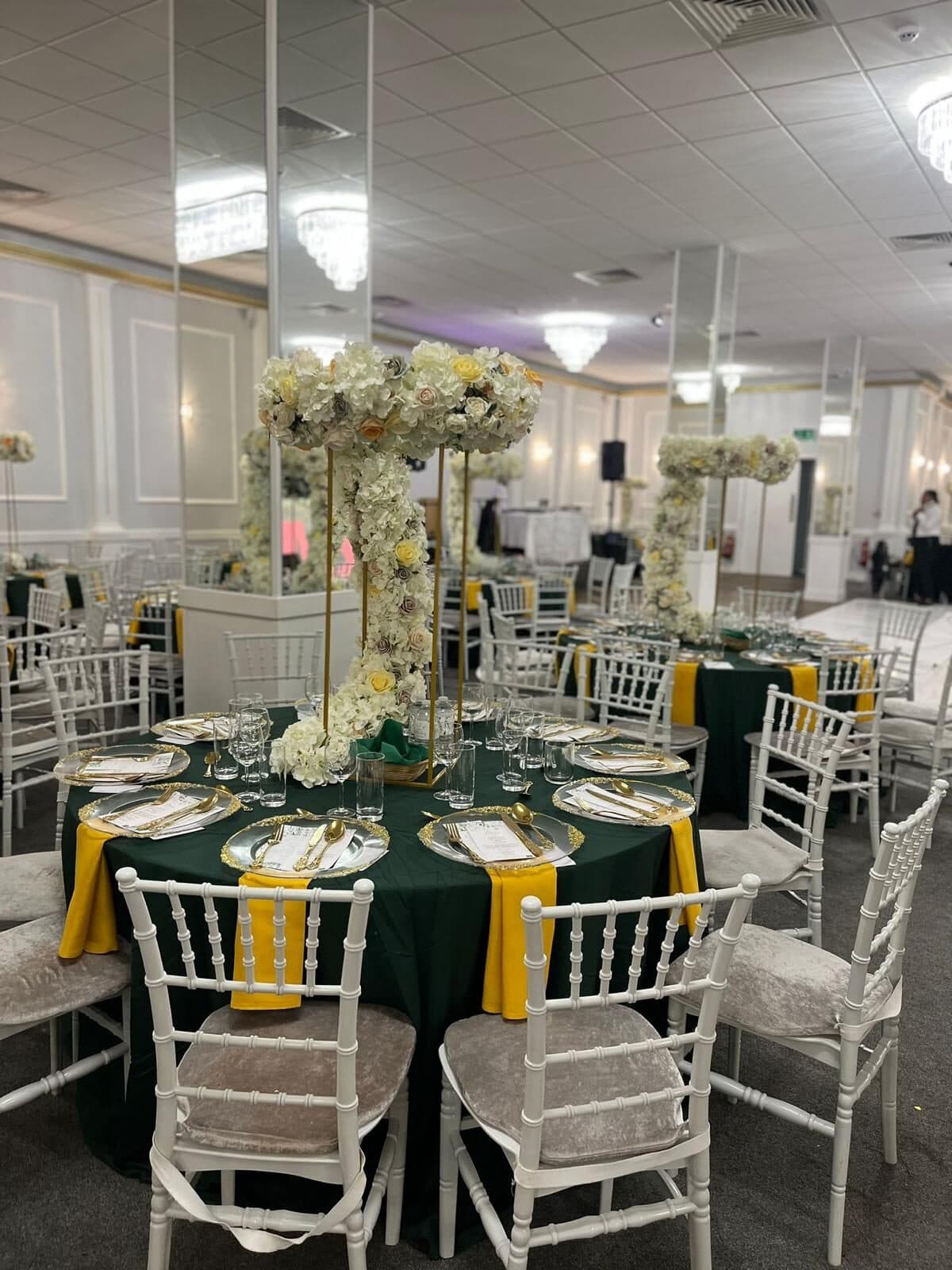 Tall white floral stand centrepieces over dark green table linen with white chiavari chairs